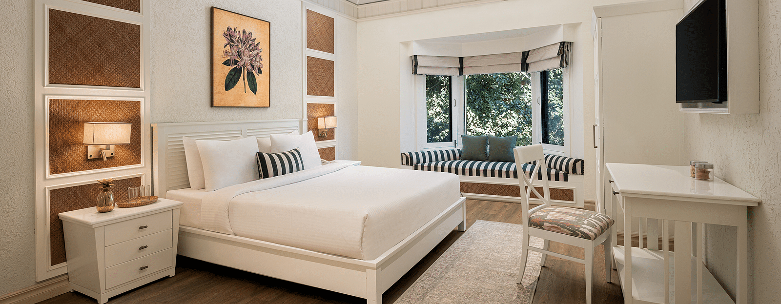An image of a bedroom with double size bed, bedside table on either side, photos hanged on the wall and four windows from which natural lights are coming in - The Riverview Retreat,  Corbett