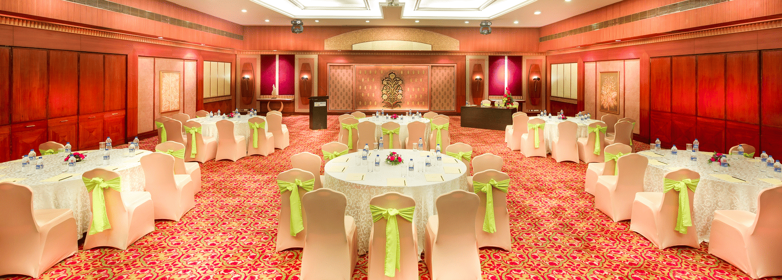 A wedding hall with white chairs tied with yellow ribbons pointing towards the stage at Grand Chennai By GRT Hotels.