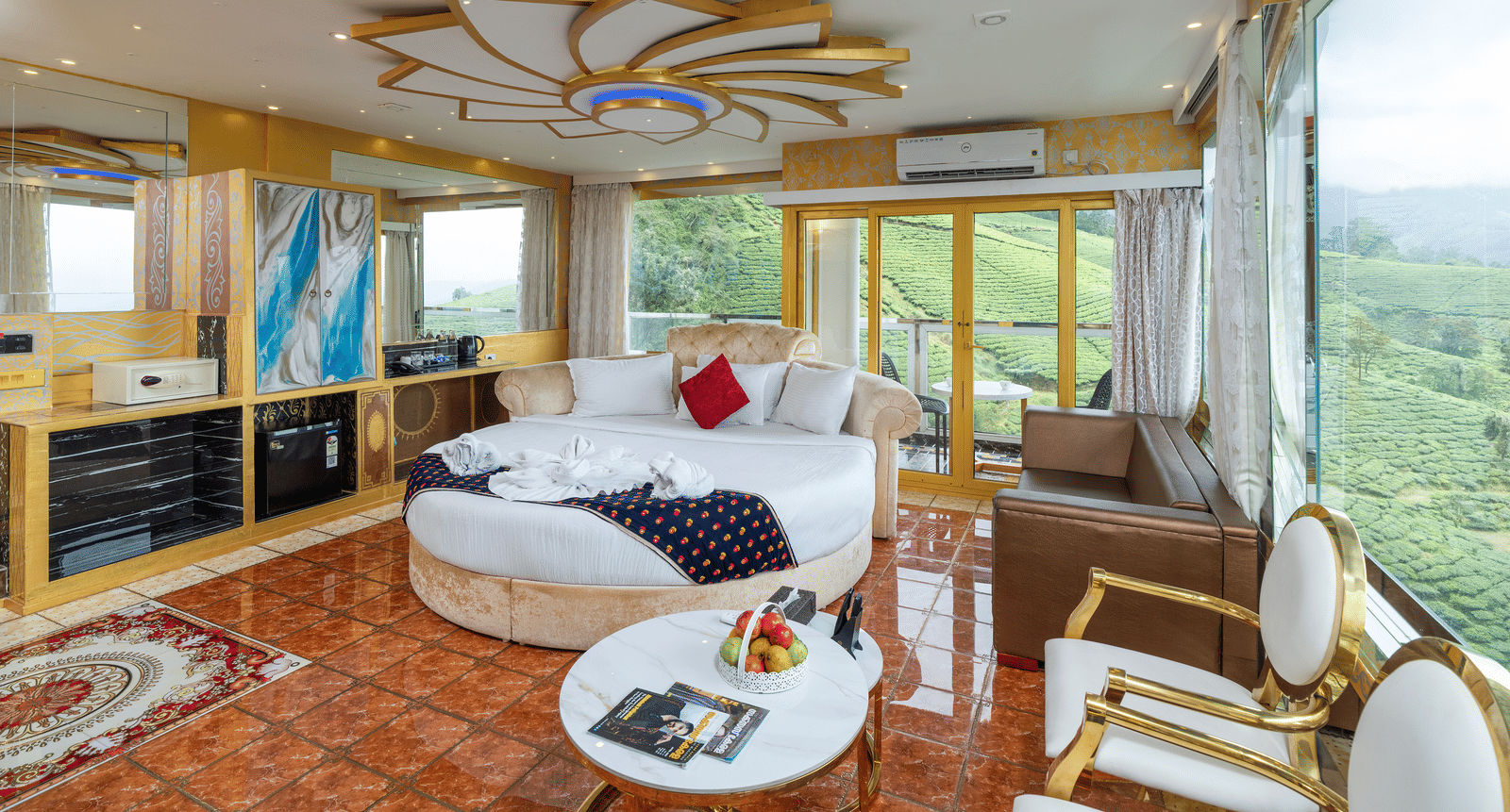 The bedroom of the Jacuzzi 180-degree Suite at Parakkat Nature Hotel and Resorts, Munnar, featuring a large bed, seating, an elaborate ceiling design, and large windows with a view of the surrounding hills.