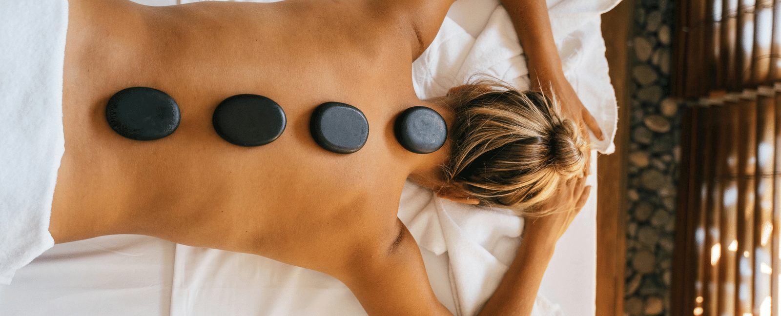 A woman lying down with back with black stones kept over her spine.