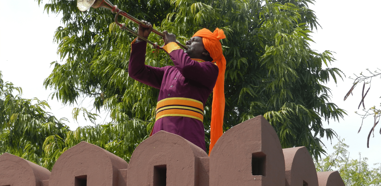 A man in traditional attire playing an instrument atop a fortified wall  - Khas Bagh, Jaipur.