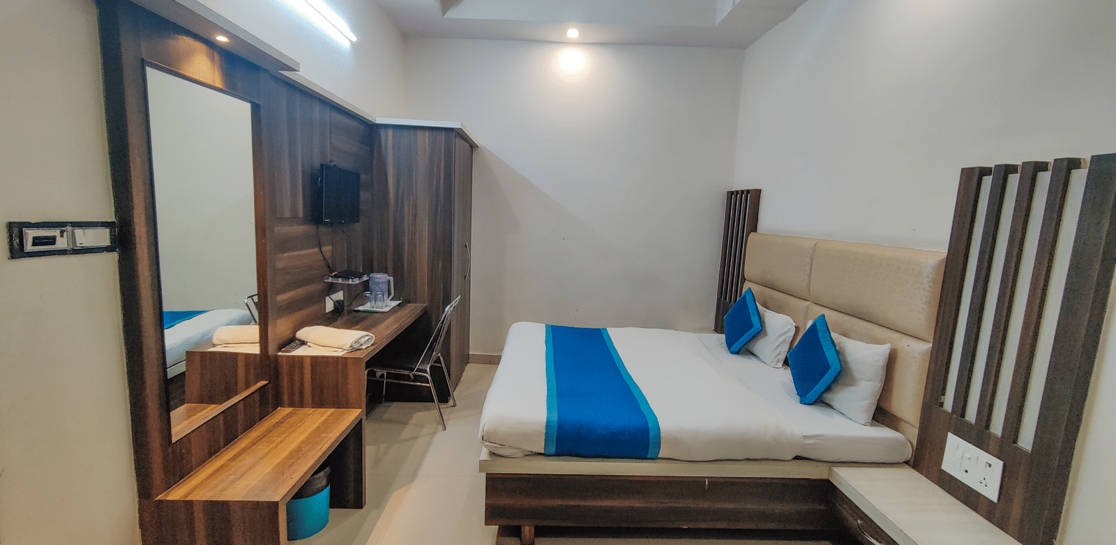 Brightly-lit hotel room featuring a large bed with a blue and white cover, wooden headboard, and a mirrored vanity area - Perfectstayz Value Grey Castle, Haridwar