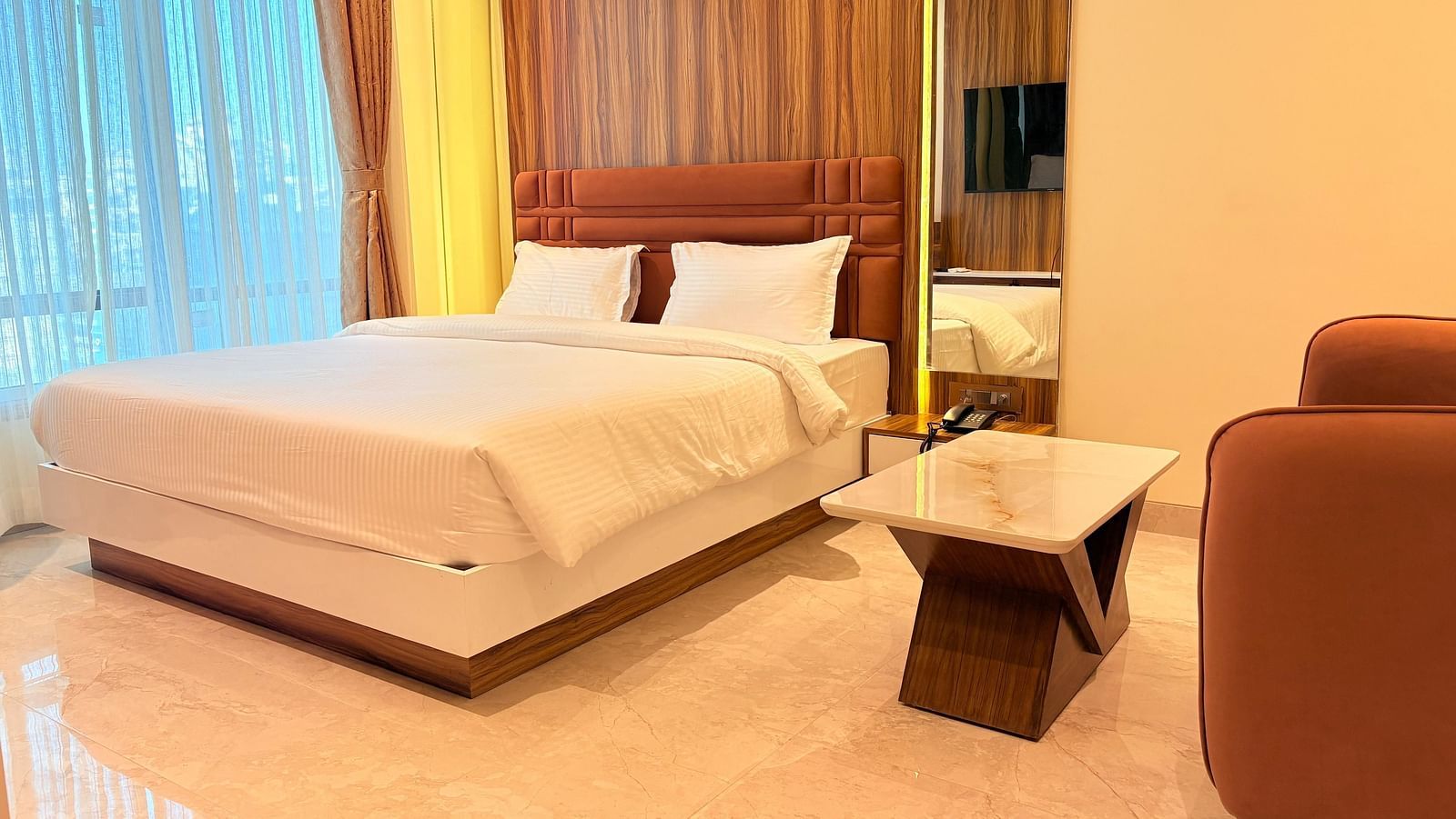 A bed with a wooden headboard and a television reflected in the mirror at Hotel Mumbai House, Vashi.