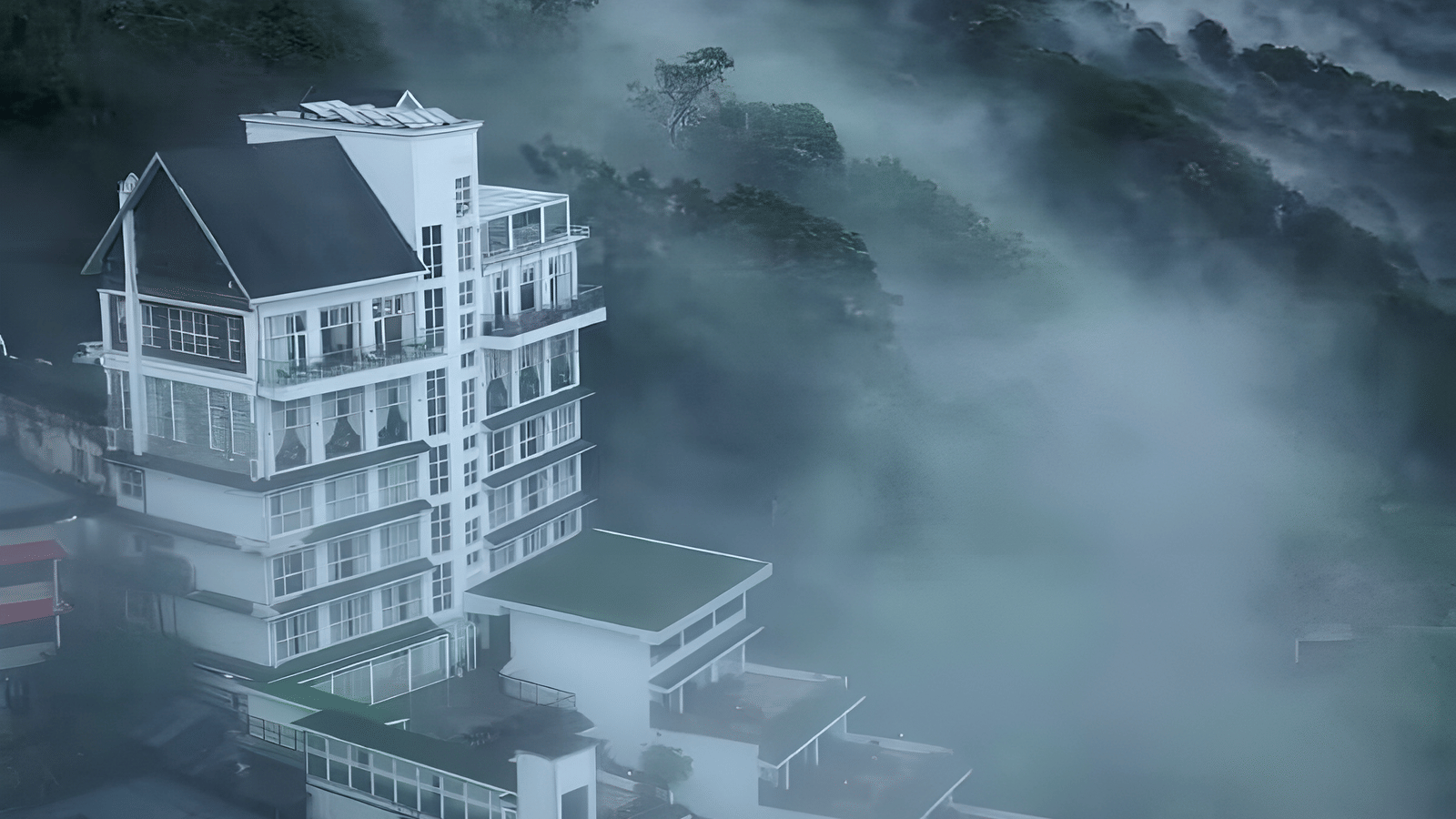 A tall, modern white and dark-roofed hotel building on a steep hillside, partially obscured by dense fog and mist.