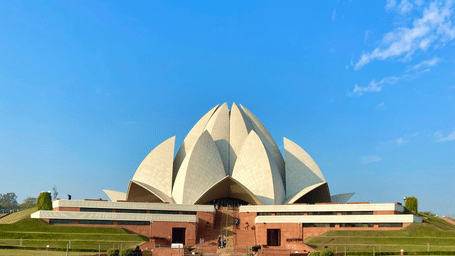A facade view of Lotus Temple (New Delhi), in the distance, with a pathway leading to it and lawn area on either side of the pathway
