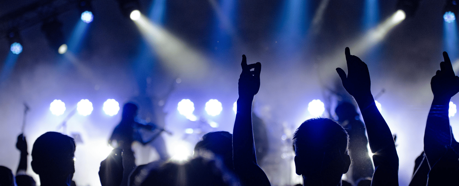 A live music performance with an audience raising hands under stage lights
