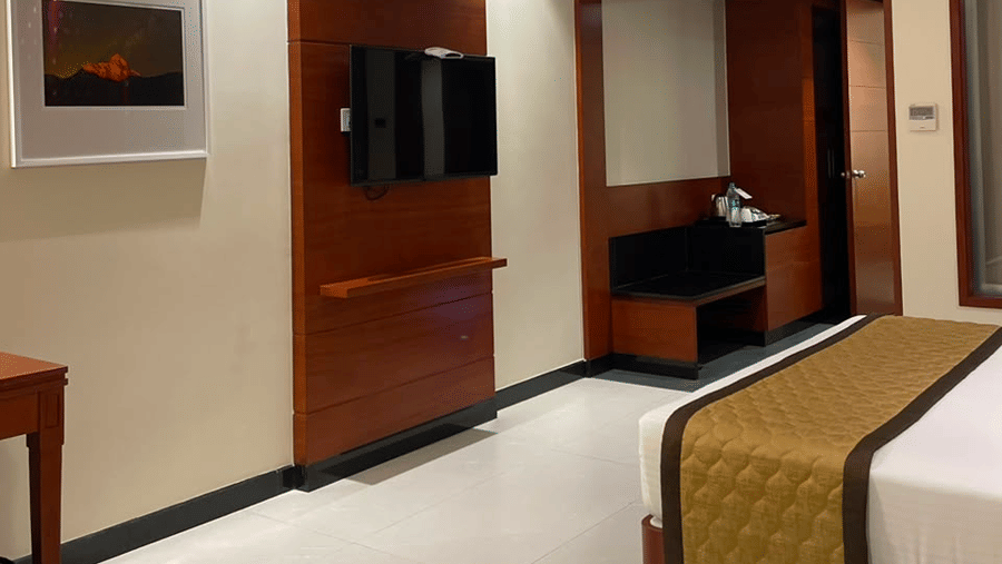 A room with a large bed, sheets, pillows, a television, and curtains. | MM Legacy, Kanchipuram