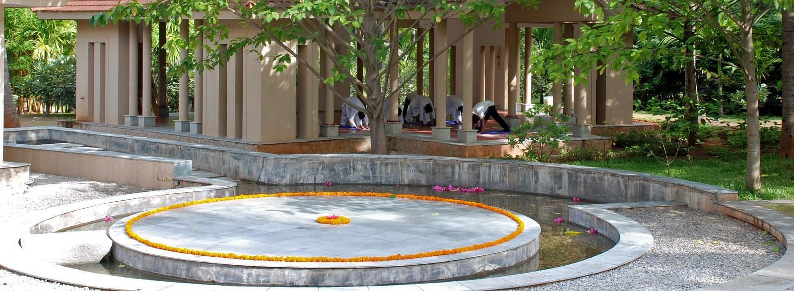 A circular feature surrounded by trees and a building with a thatched roof, outdoor setting - Shreyas Retreat