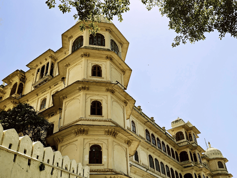 Low-angle view of Udaipur City Palace's tower and stonework, framed by tree branches