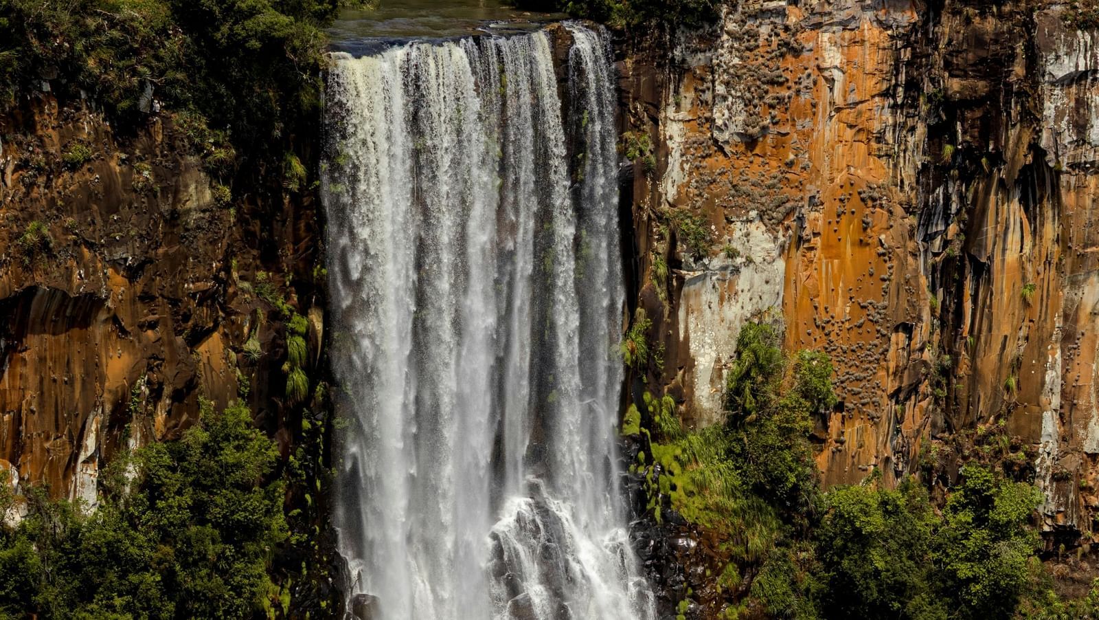 Waterfall cascading down a cliff surrounded by greenery.