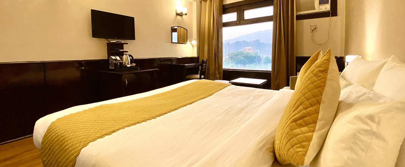 Side view of a bedroom with warm yellow lights highlighting the walls around a mounted television, at DLS Park Grace, Haridwar.
