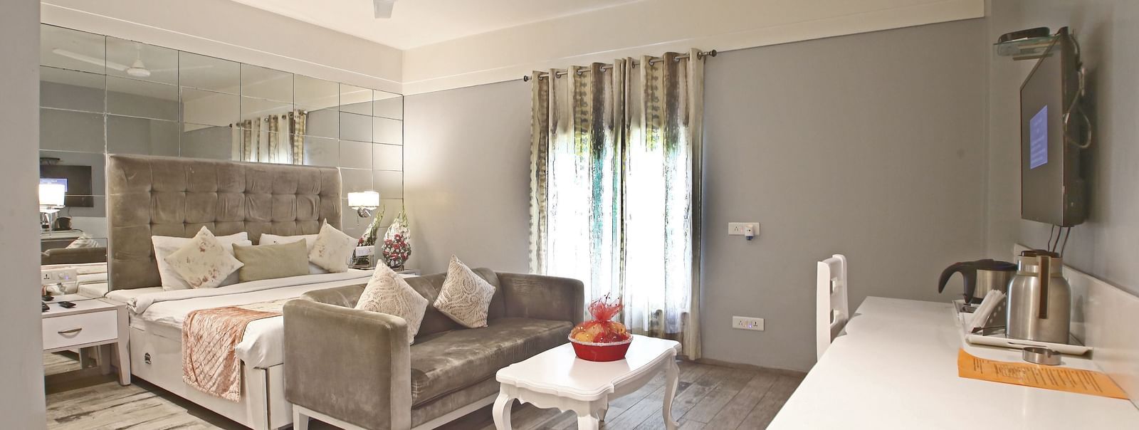 Elegant room with a large bed and a sofa in front, table, chairs, and TV unit at Hotel Emerald, Chandigarh