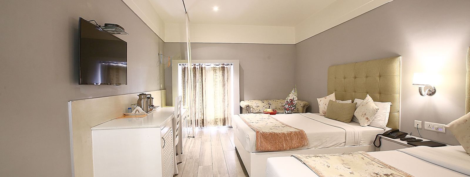 Elegant room with two large beds, table, chair and TV unit at Hotel Emerald, Chandigarh