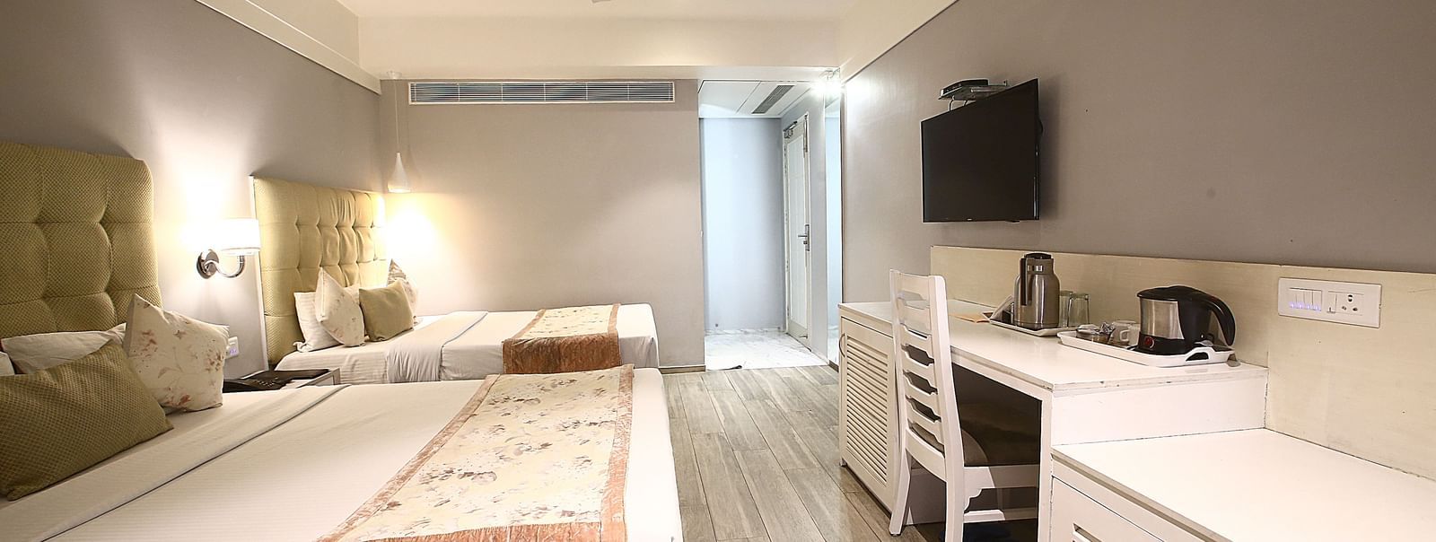 Elegant room with two large beds, table, chair and TV unit at Hotel Emerald, Chandigarh
