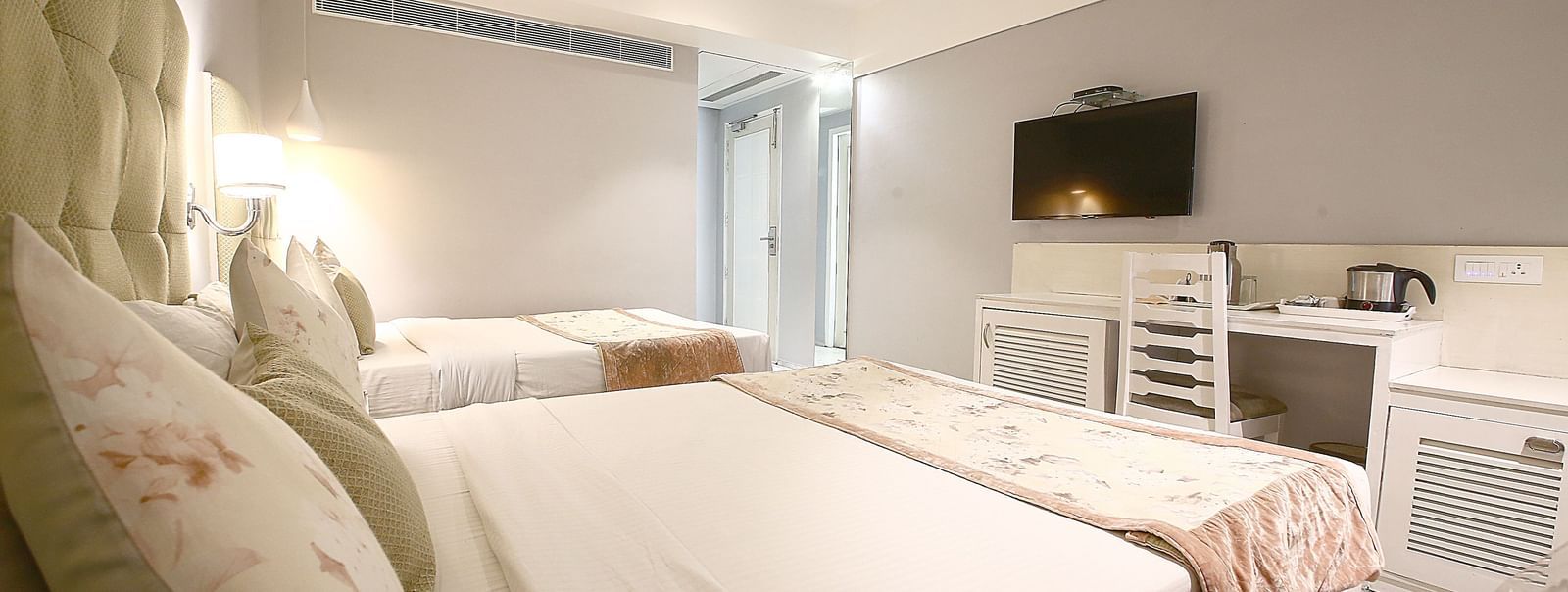 Elegant room with two double beds, table, chair and TV unit at Hotel Emerald, Chandigarh