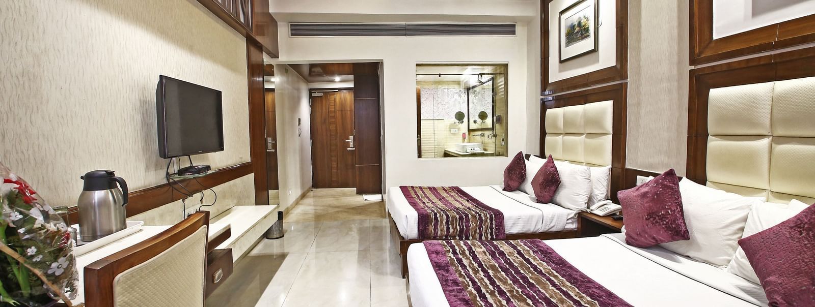 Elegant room with two large beds, table, chair and TV unit at Hotel Emerald, Chandigarh