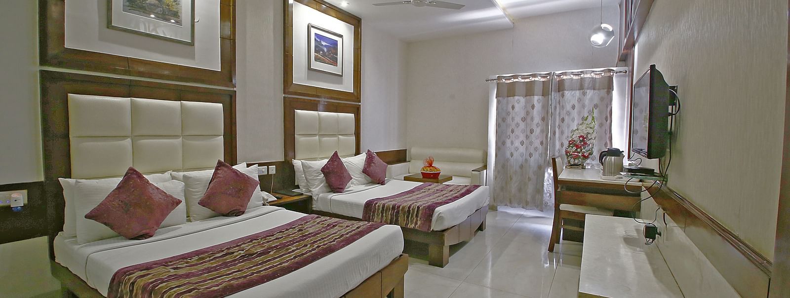 Elegant room with two large beds, table, chair and TV unit at Hotel Emerald, Chandigarh