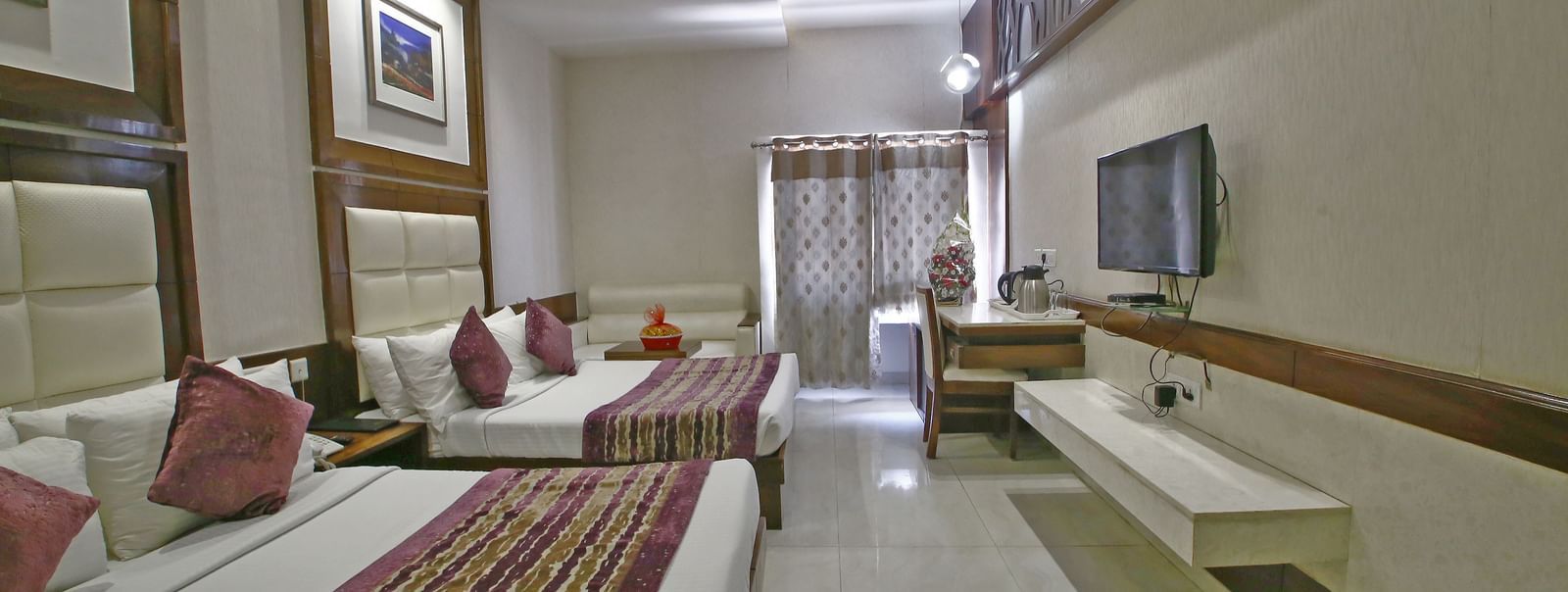 Elegant room with two large beds, table, chair and TV unit at Hotel Emerald, Chandigarh