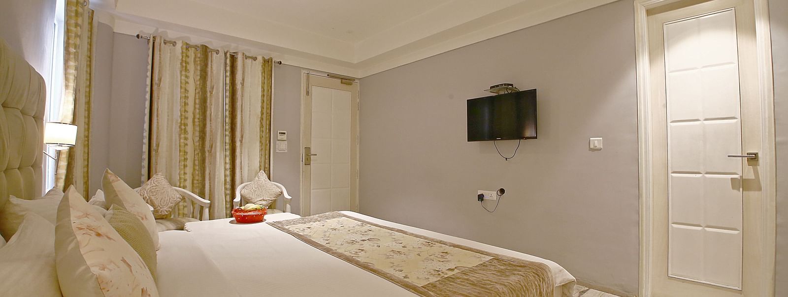 Elegant room with a large bed, chairs, and TV unit at Hotel Emerald, Chandigarh