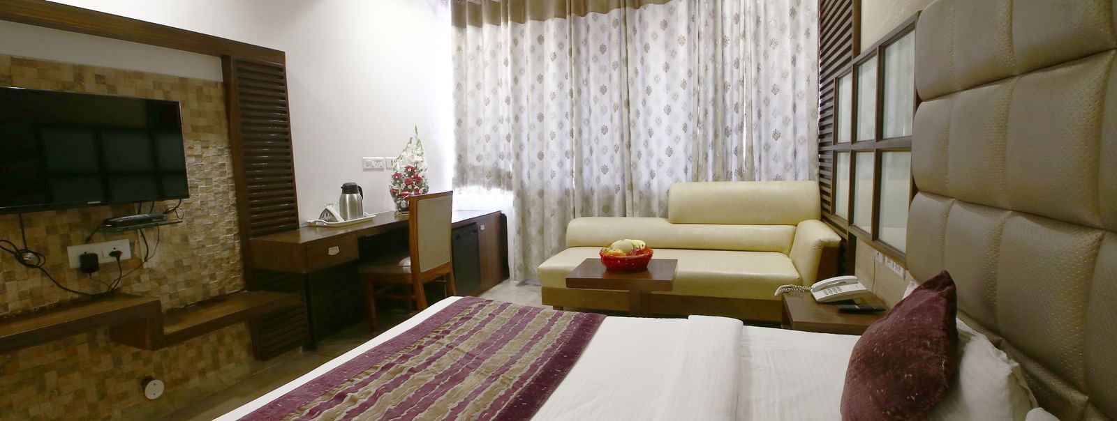 Elegant room with a large bed, table, chair, and TV unit at Hotel Emerald, Chandigarh