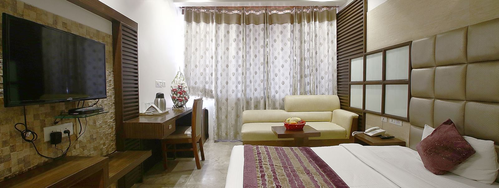 marble floored modern room with a large bed, table, chair and TV unit at Hotel Emerald, Chandigarh