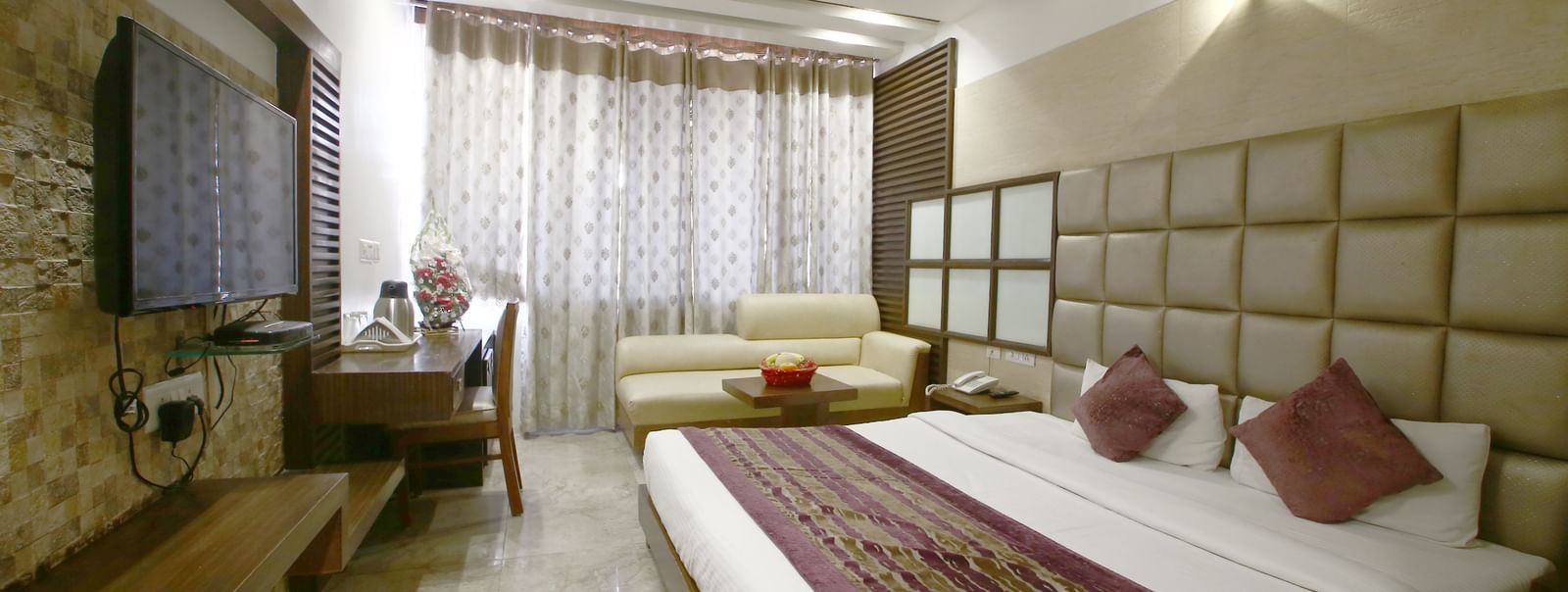 marble floored modern room with a large bed, table, chair and TV unit at Hotel Emerald, Chandigarh