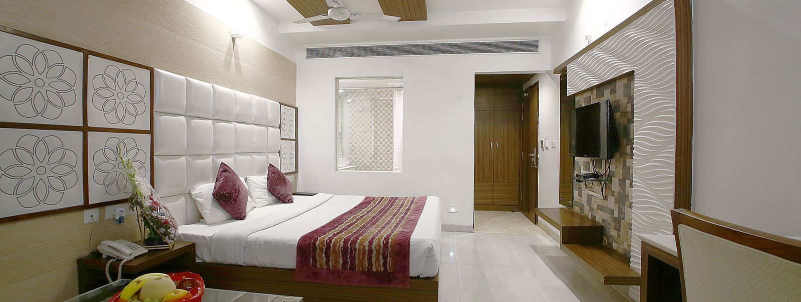 Elegant room with a large bed, table, chair, and TV unit at Hotel Emerald, Chandigarh