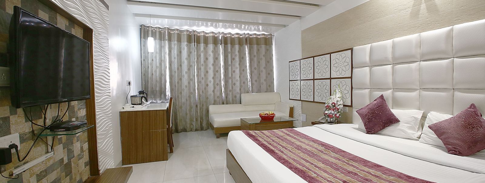Elegant  well furnished room with a large bed, table, chair, sofa and TV unit at Hotel Emerald, Chandigarh