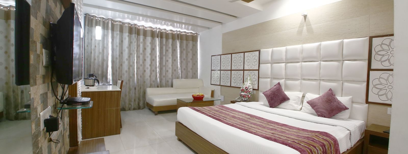marble floored modern room with a large bed, table, chair and TV unit at Hotel Emerald, Chandigarh