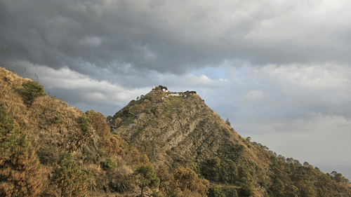 A house on top of a mountain with trees and clouds in the background. 