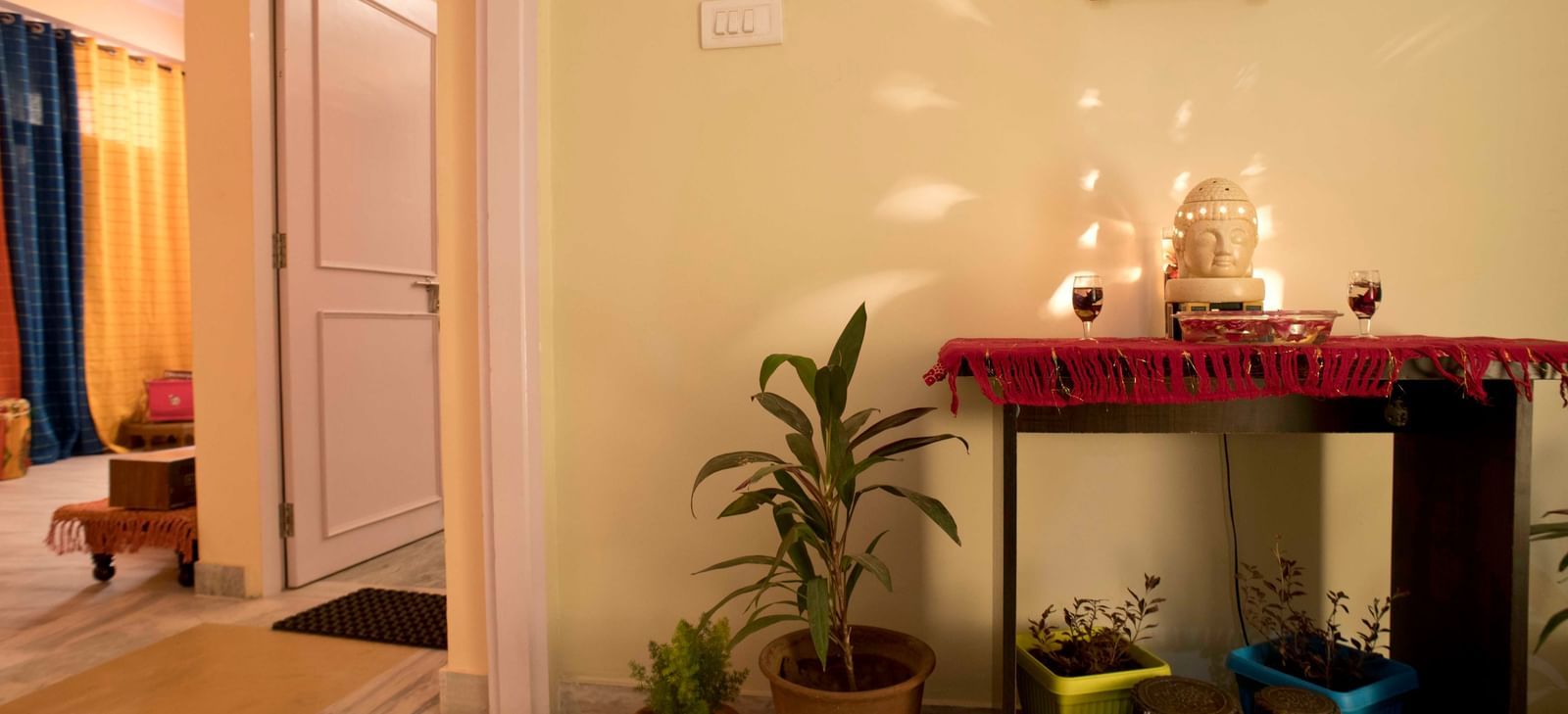 An indoor shrine with lit lamps, small plants, and decorative items on a shelf against the wall at Jaypore360 Homestay in Jaipur.