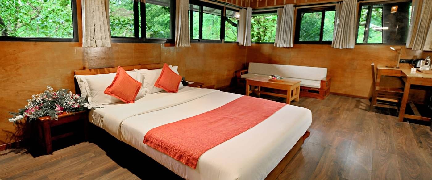 Room with multiple windows and a bed, offering lush forest views at Vythiri Resort, Wayanad