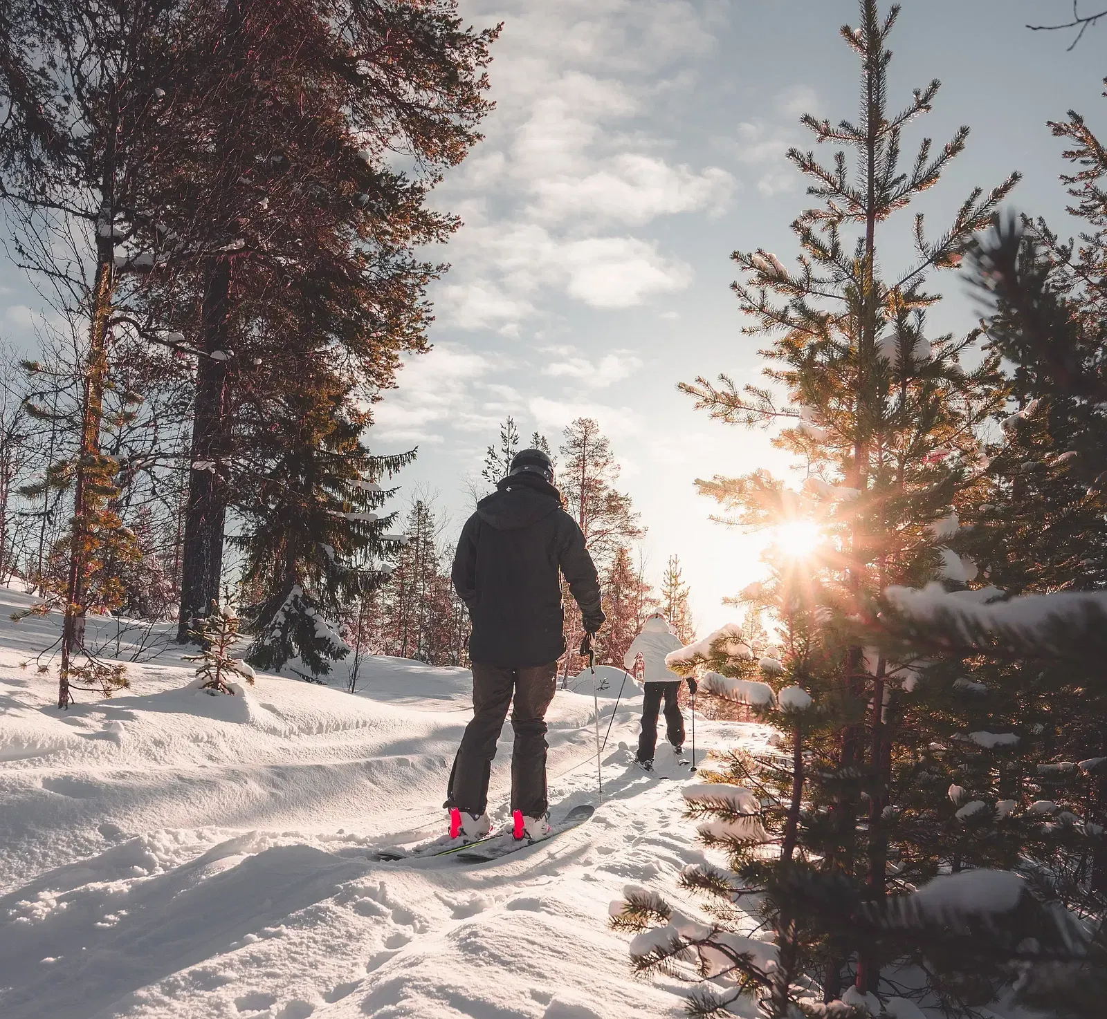A person walks on a snowy path through a forest towards a bright sunburst.