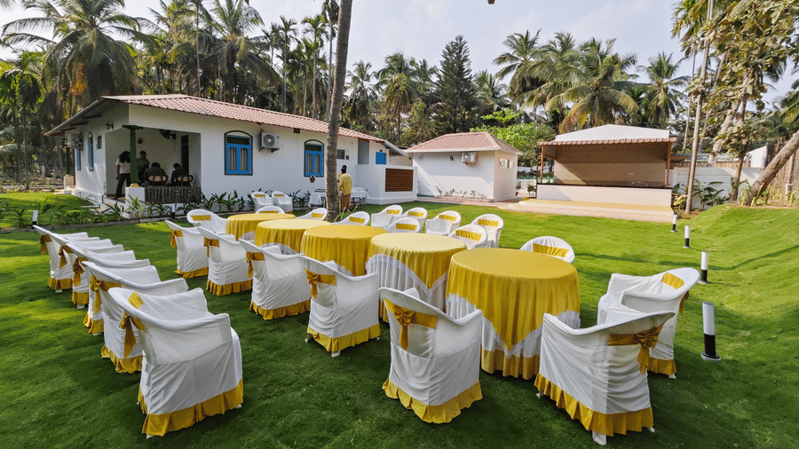 Tables and chairs arranged in the wedding lawn with trees in the backdrop at Ibex Resorts, Coimbatore (Kakarla).