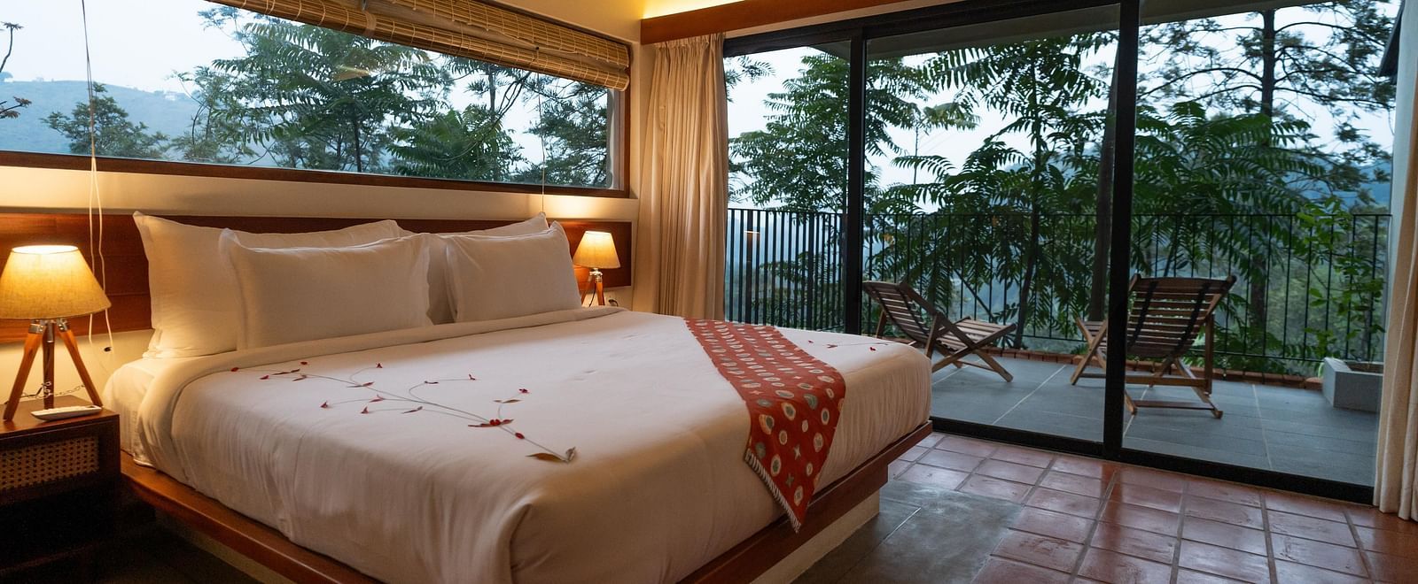  A well-appointed bedroom at Vaasta Vagamon featuring a large bed with a decorative runner, and expansive windows overlooking a scenic view.
