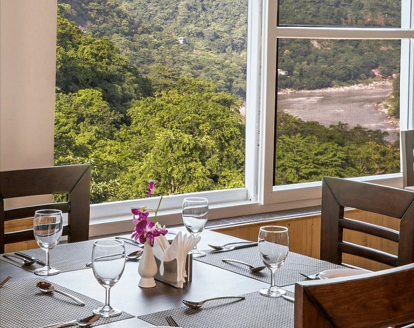 A close up shot of a dining table with table mats and glassware with a huge window behind it at Regenta Inn DLS.