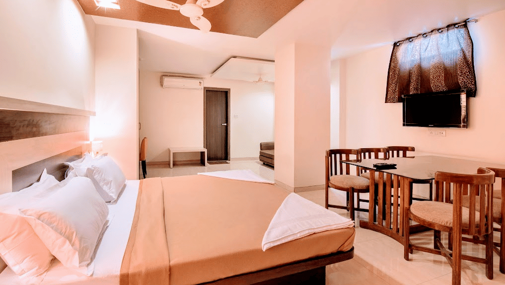 Suite room containing a double bed, small dining table with chairs, and wall-mounted television screen.