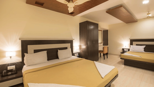 A room with two neatly made beds positioned a short distance apart, featuring a wardrobe, a vanity area, and a ceiling fan.