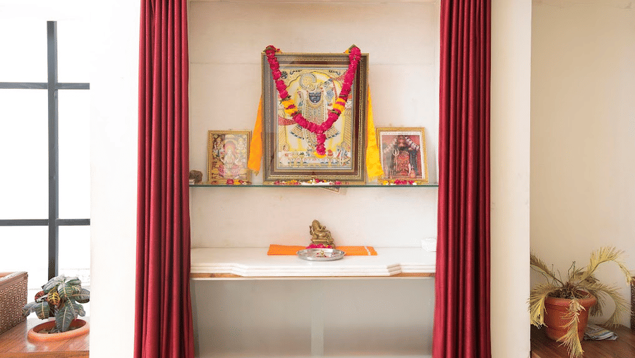 A small indoor prayer shrine or mandir area inside the hotel decorated with framed pictures and red curtains.