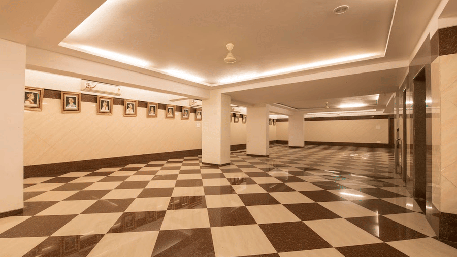 Long perspective of an empty function hall with recessed warm ceiling strip lights and checkered floor tiling.