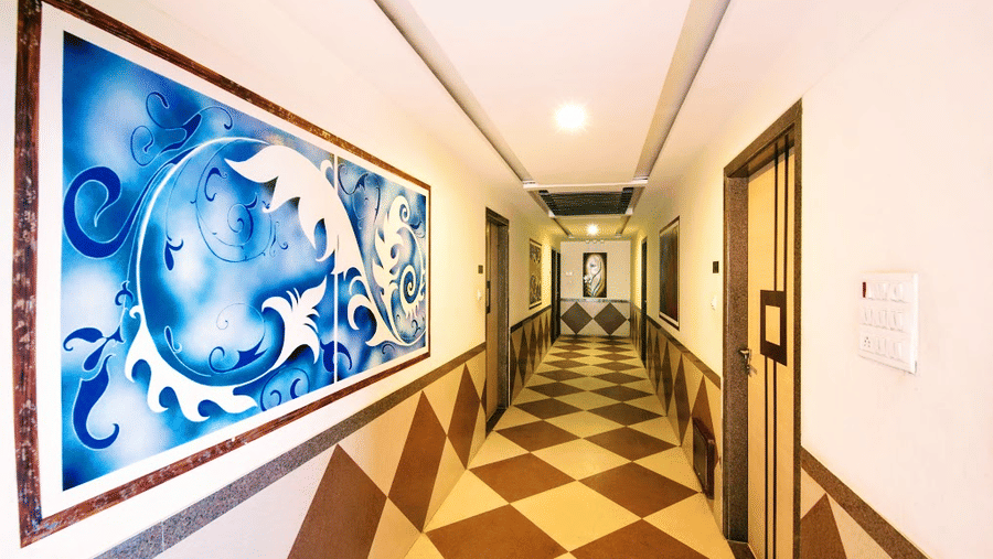 A long hotel hallway corridor with diamond-pattern floor tiles and a large blue canvas painting on the left wall.