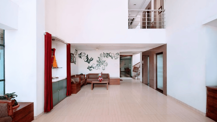 Wide view of an open-plan hotel suite lounge featuring high ceilings, a loft balcony, and a brown sofa set.