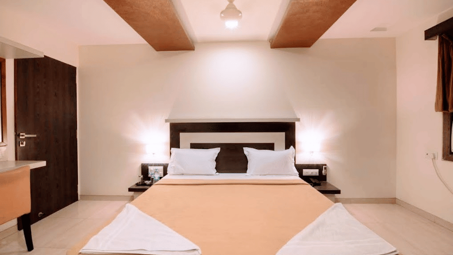 front view  of a modern hotel double bed with cream-colored bedding and decorative folded towels.