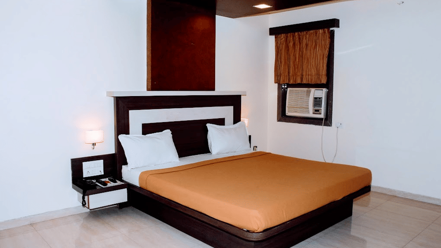 executive room featuring a double bed with a brown runner, window air conditioner, and warm light.