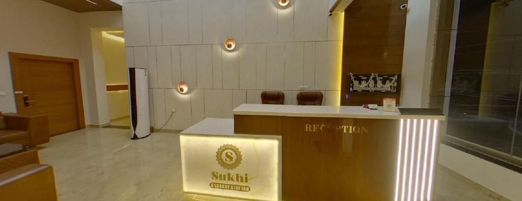 Reception area with a wooden desk featuring an illuminated logo, set against a backdrop of textured walls and ambient lighting.- Sukhi - A Luxury Stay Inn, Chikkamagaluru