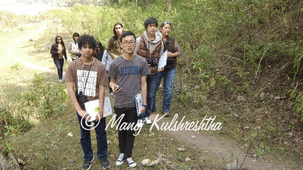 A group of young people hiking together along a dirt trail in a grassy, wooded outdoor area.