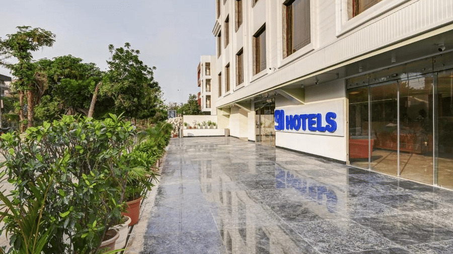 A marble-clad driveway in front of the entrance to Hotel 91 Privé, Gurugram, with several lush green potted plants on the other side.
