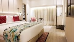 Elegant hotel room with a king size bed, red accent pillows, sheer curtains, cosy seating by the window, pendant lights, and warm ambient lighting - Golden Tulip, Lucknow