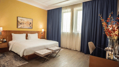 Well-lit bedroom with a king-size bed, desk, chair, and decorative elements at La Maison Hotel, Doha.