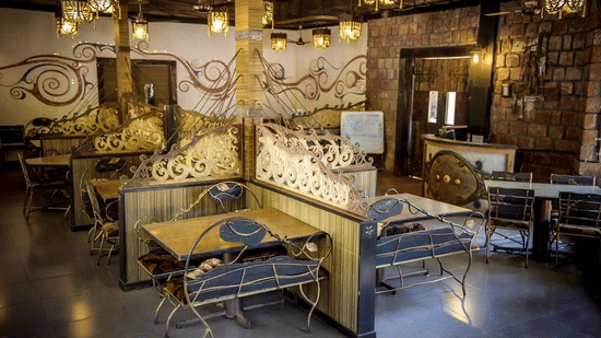 An indoor restaurant dining hall featuring decorative wooden booth partitions, tables, chairs, and warm ambient lighting.